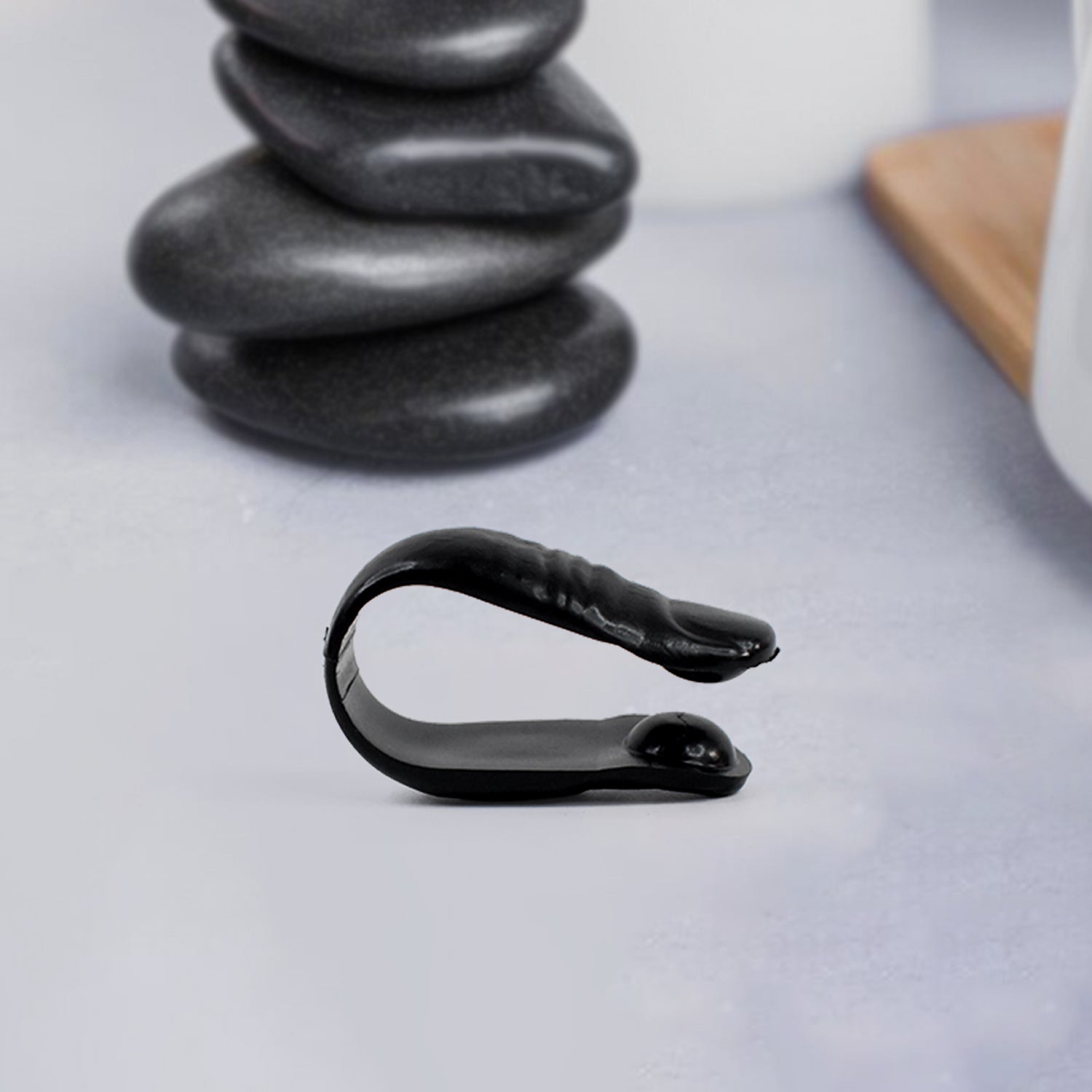 black curved portable sugar control acupressure device on tabletop near stacked spa stones and mug