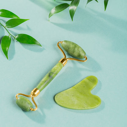 natural jade facial roller for glowing skin with gua sha tool on mint background with leaves