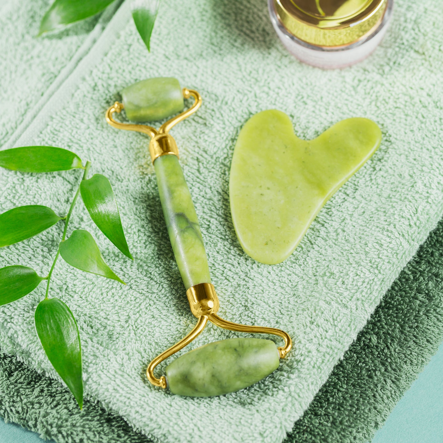 natural jade facial roller for glowing skin with gua sha tool on green towel spa setup
