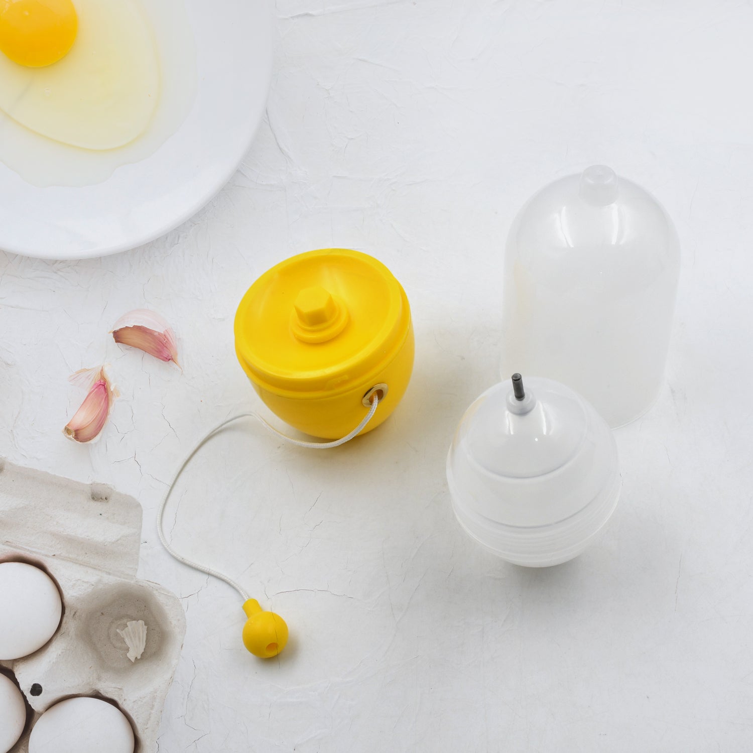 household egg puller gadget set yellow and white with suction cups next to cracked egg and carton