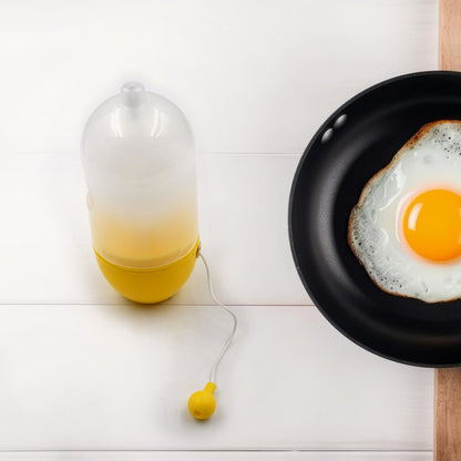 household egg puller gadget in yellow with pull cord next to frying pan holding a sunny side up egg