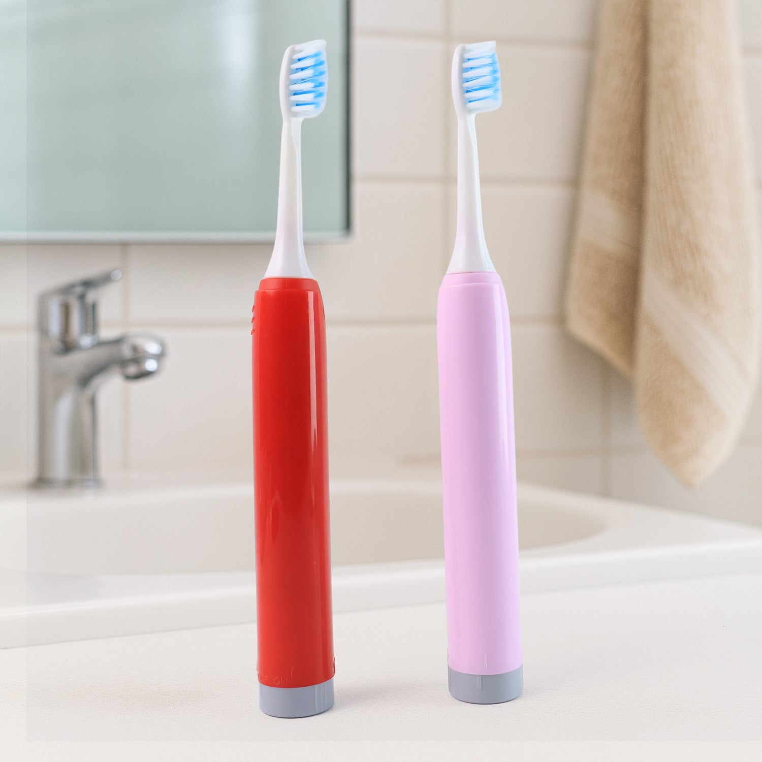 red and pink battery toothbrushes standing on bathroom sink counter with blue bristles best battery toothbrush for adults