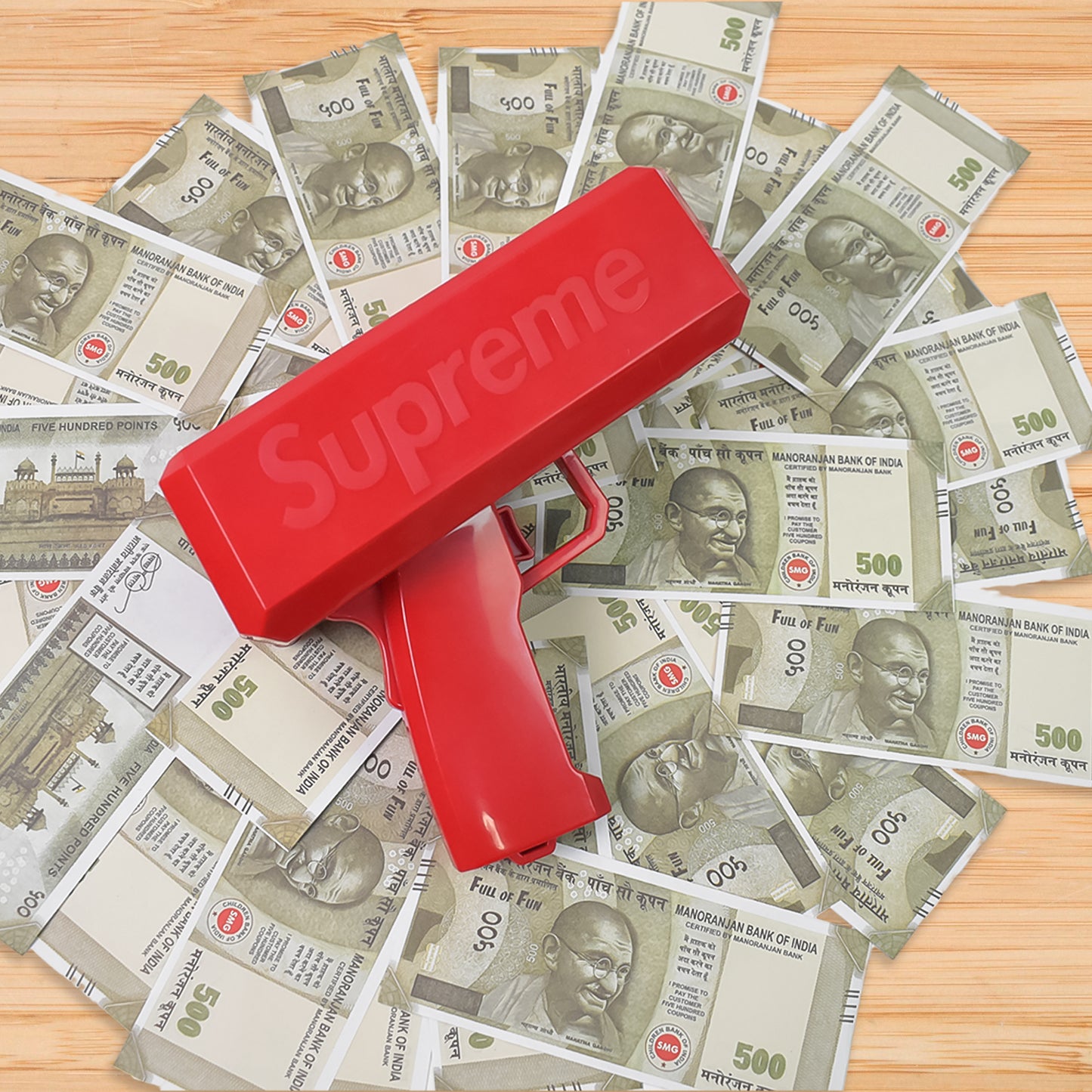 red toy money gun shooter for parties on scattered Indian 500 rupee notes wooden table