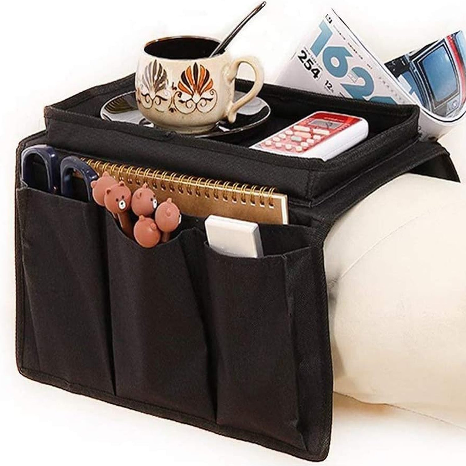 black sofa armrest organizer storage bag with multiple pockets and flat tray holding remote phone notebook and cup